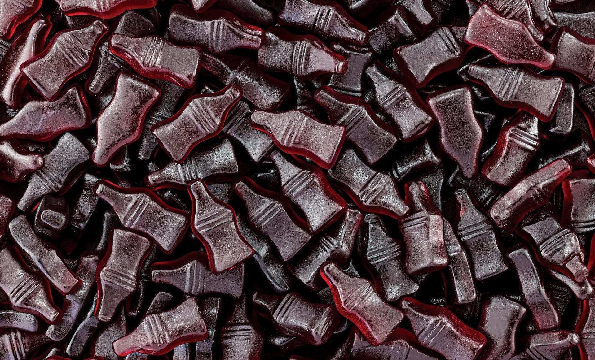 Dark red flat lay of a cola bottle and gummy sweets. Distinctive styled product photography that AI cannot replicate from a generic prompt.