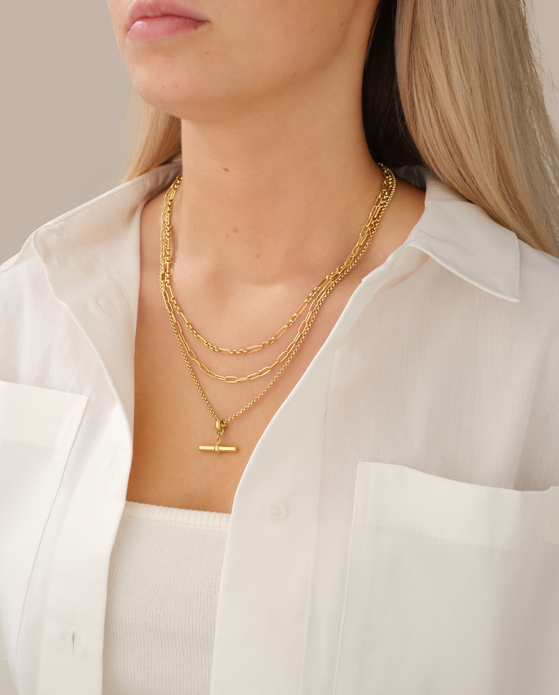 Layered gold chains and a T-bar pendant worn with a white shirt